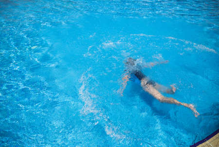 Top view of young kid swimming underwater in sunny summer pool outdoors at hotel resort. Horizontal color image.の写真素材