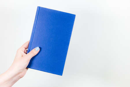 Closeup view of female hand holding blue paper book isolated on white background. Horizontal color photography.の写真素材