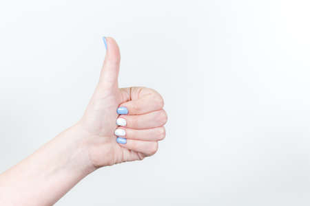 Closeup view of female young hand in likeness gesture with thumb up isolated on white background. Fingernails with white and blue professional modern gel polish.の写真素材