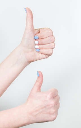 Closeup view of two female hands in likeness gesture with thumb up isolated on white background. Fingernails with white and blue professional modern gel polish.の写真素材
