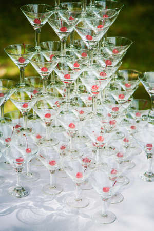 Pyramid of many empty glasses with red cherries inside of them. Outdoors party celebration of holiday or wedding. Catering service. Vertical color photography.の写真素材
