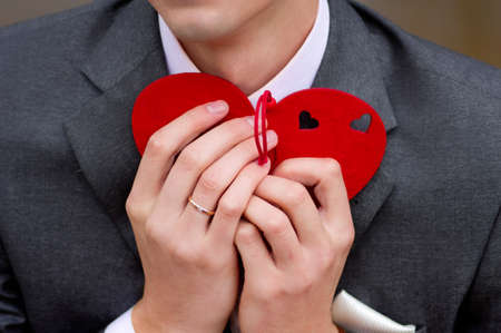 Closeup view of two hands of young european white man holding cute red heart. Happy Valentine day. Horizontal color photography.の写真素材