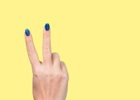 Woman holding hand with two fingers up making v sign. Female hand isolated on yellow background....