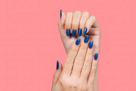 Closeup view of beautiful female hands with blue glossy professional manicure isolated on pink...