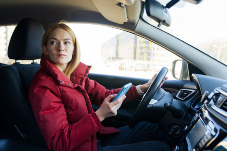 A young woman is typing on her phone while sitting in a car