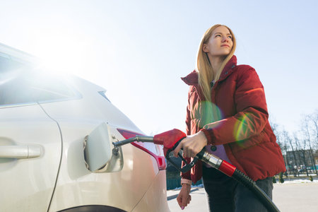 A beautiful young woman refuels her car and types on her phoneの写真素材