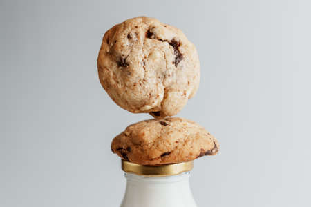 Cookies with pieces of chocolate lying on a bottle of milk on a white backgroundの写真素材