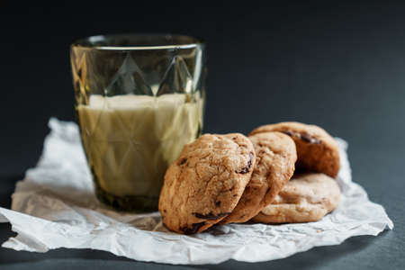 Homemade cookies with pieces of chocolate next to a glass of milk on a dark backgroundの写真素材