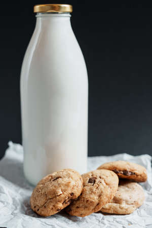 Homemade cookies with pieces of chocolate next to a bottle of milk on a dark backgroundの写真素材