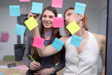 Two female colleagues write company plans on colorful stickersの写真素材