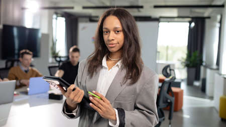 Portrait of a young african american woman with a laptop in her hands on the background of the officeの写真素材