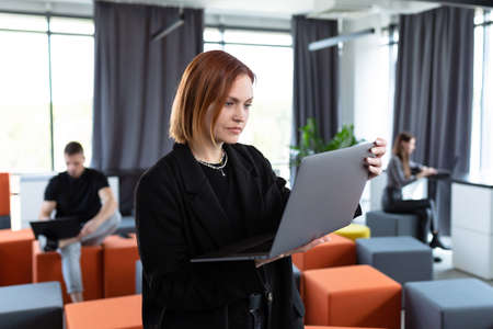 A young woman with a laptop on the background of a working officeの写真素材