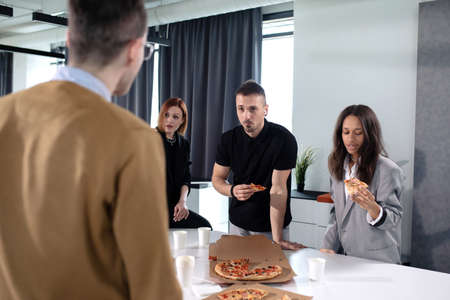 Colleagues eat pizza at the office during lunchの写真素材