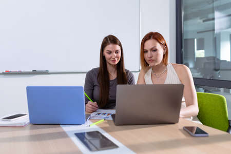 Two young women are working on a project in a meeting room
