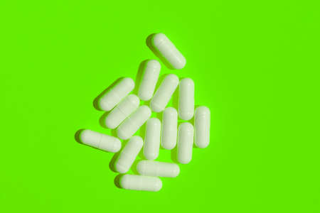 White pills on a bright green background. Vitamins, healthy lifestyle. flat lay