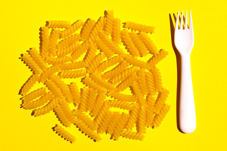 Raw pasta next to a fork on a yellow background. flat lay
