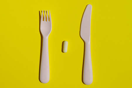 Fork and knife between which lies a white tablet on a yellow background. The concept of unhealthy food. flat layの写真素材