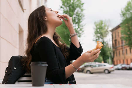 A young woman is sitting in a summer cafe. Breakfast outside with croissant and coffee. summer vibe