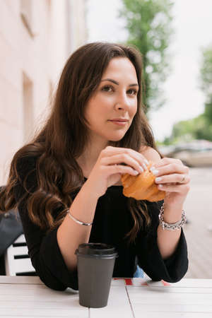 Portrait of a young woman sitting in a summer cafe and eating a croissant with coffee. good mood and rest in summerの写真素材