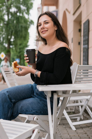 A young woman is eating a croissant and drinking coffee. Summer cafe, breakfast outsideの写真素材