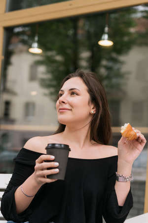 Breakfast in a summer cafe. A young woman is sitting at a table and eating a croissant with coffee