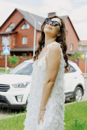 A young woman during a walk through a beautiful cottage village. A model in a white dress and sunglassesの写真素材
