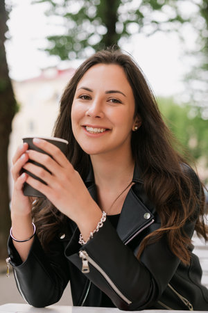 A young woman drinks coffee from a paper cup outsideの写真素材