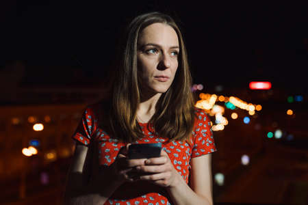 A young woman is typing on her phone against the background of an evening cityの写真素材
