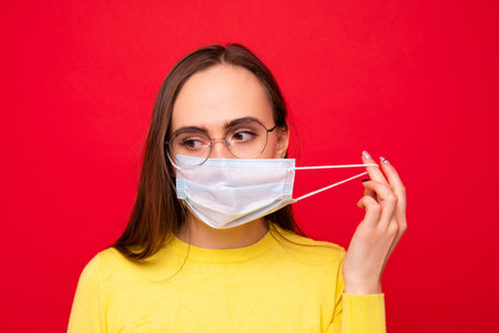 Portrait of a young woman wearing glasses and a protective mask on a red backgroundの写真素材