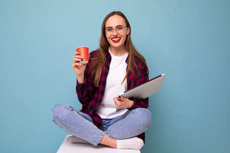 A young woman sits with a laptop and drinks coffeeの写真素材