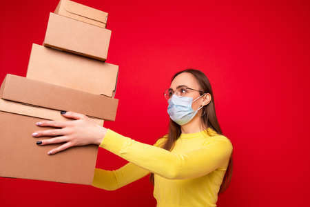 A young woman in a protective mask holds cardboard boxes for moving on a red backgroundの写真素材