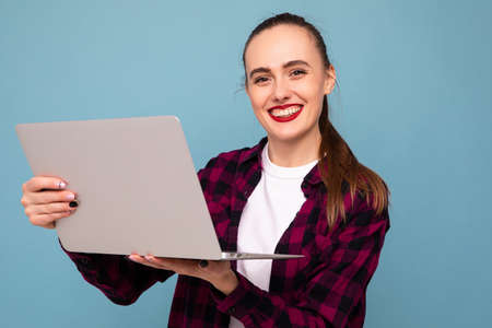 A young woman in a plaid shirt is typing on a laptopの写真素材