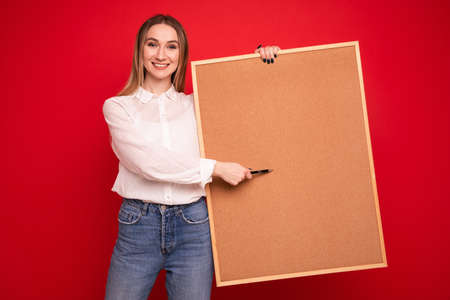Portrait of a young woman in a white shirt holding a task board on a red backgroundの写真素材