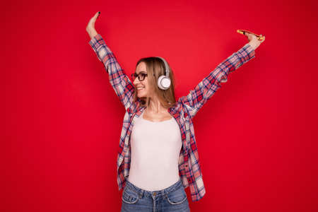 A happy young woman listens to music with headphones from her phone on a red backgroundの写真素材
