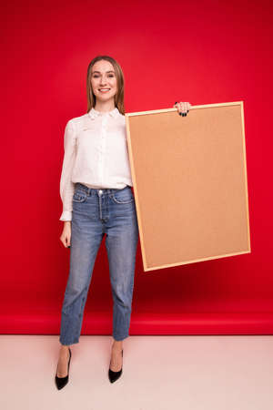 Portrait of a young woman in a white shirt holding a task board on a red backgroundの写真素材