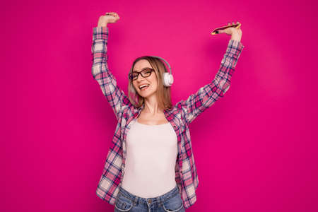 A happy young woman listens to music with headphones from her phone on a pink backgroundの写真素材
