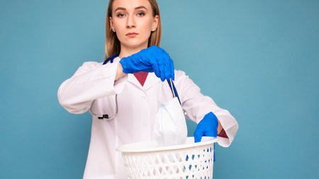A female doctor throws a used medical mask in the trashの写真素材