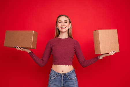 A young woman holds two cardboard boxes on a red backgroundの写真素材
