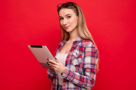 A pretty young woman in stylish clothes holds a tablet on a red backgroundの写真素材