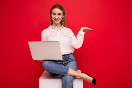 Young woman in a white shirt making a video call from a laptop on a red backgroundの写真素材