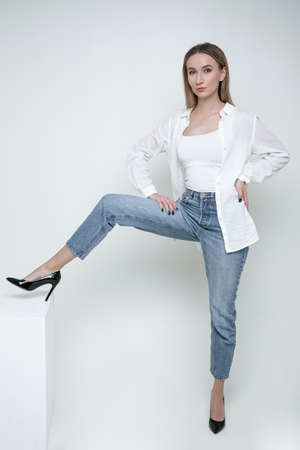 A stylish young woman in jeans and a white shirt poses in the studioの写真素材