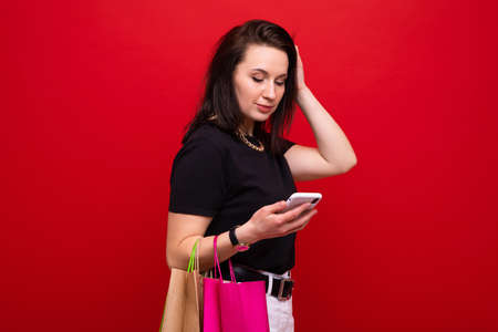 A young woman with a shopping bag and a phone in her hand on a red backgroundの写真素材
