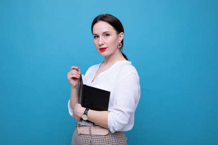 Young brunette woman with a diary and pen on a blue backgroundの写真素材