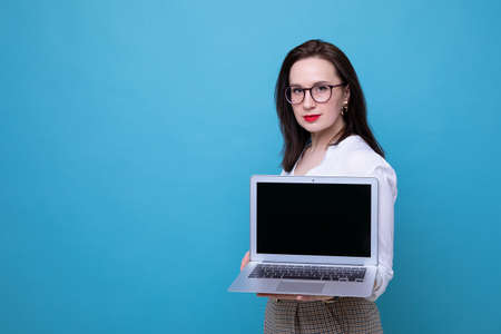 Portrait of a young brunette woman with a laptop on a blue background