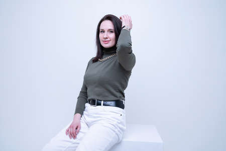 A young brunette woman in a dark golf and light jeans poses in the studio