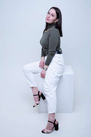 A young brunette woman in a dark golf and light jeans poses in the studioの写真素材