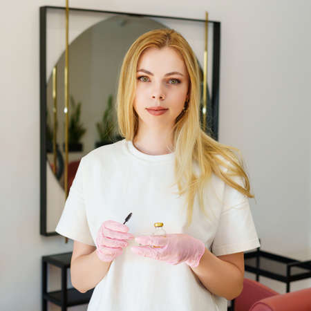 Portrait of a beauty master in a beauty salon. A young woman in a white T-shirt holds a brush and...