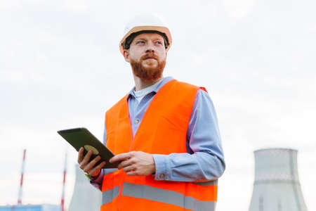 A successful professional. The man is an engineer in a helmet and a protective orange vest. Tablet...