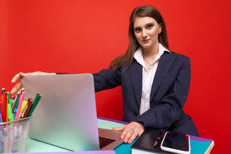 Young woman in business clothes working at a laptop on a red backgroundの写真素材