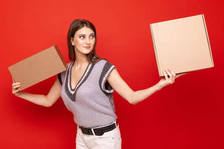 A young woman holds two cardboard boxes on a red background